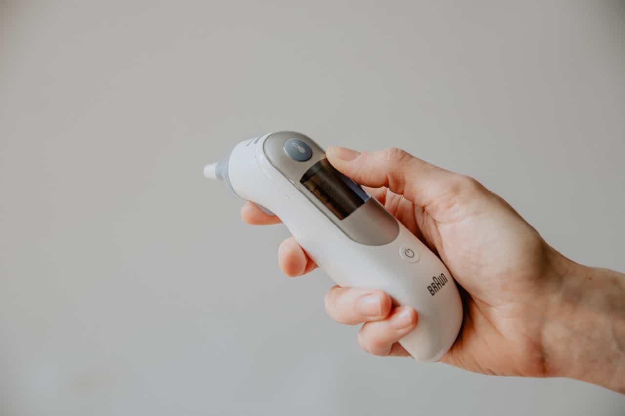 A hand holding an ear thermometer.
