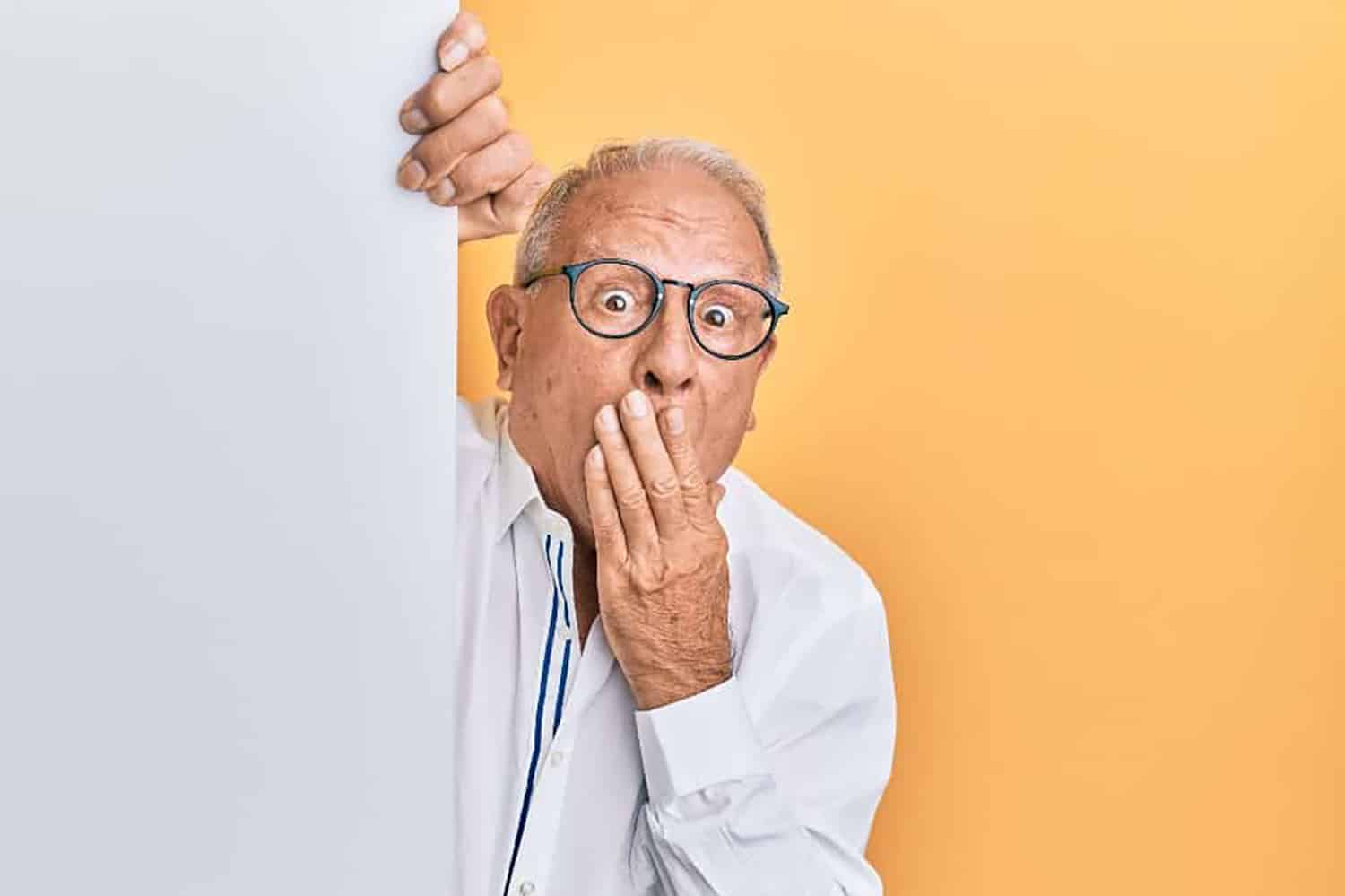 A man behind a white wall with hand over his mouth in surprise.