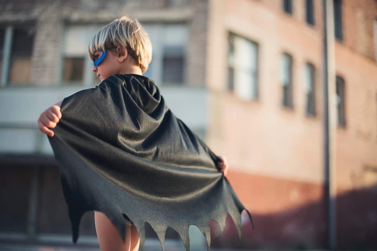 A little boy with a hero cape and mask.