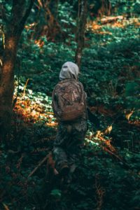 A person walking through the woods in camo with a backpack.