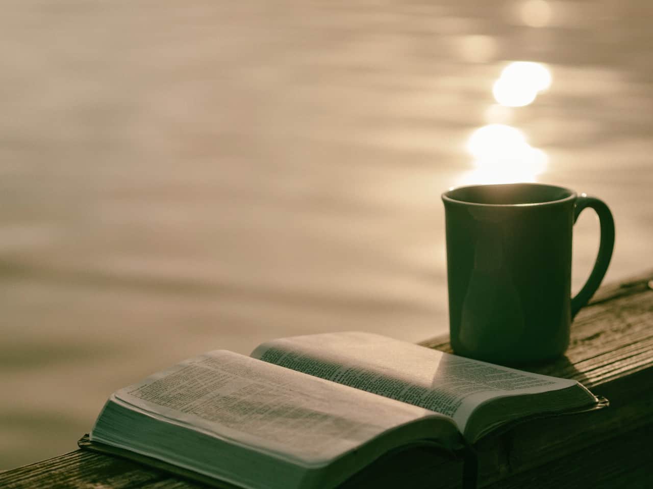 An open Bible and cup of coffee overlooking water.