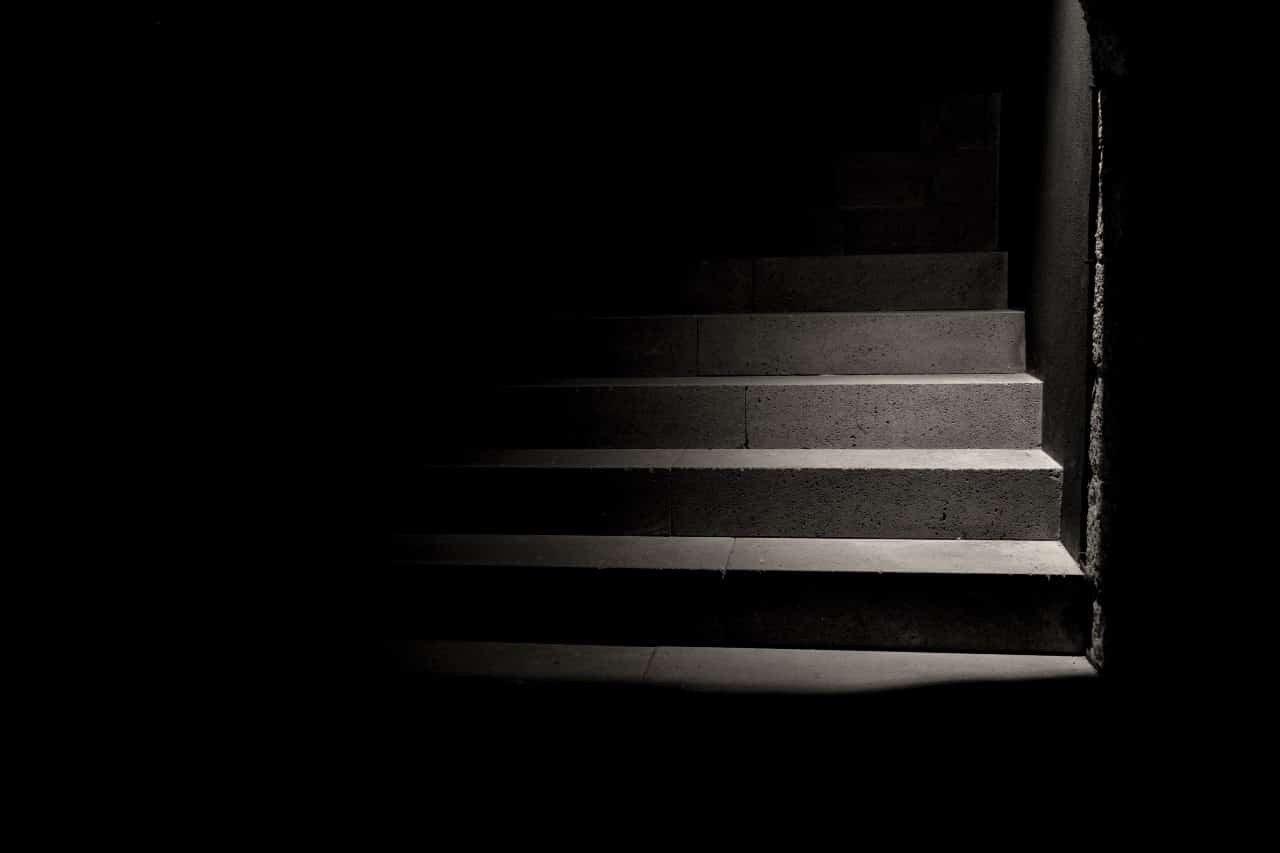A dark staircase with a small amount of light illuminating part of the stairs.