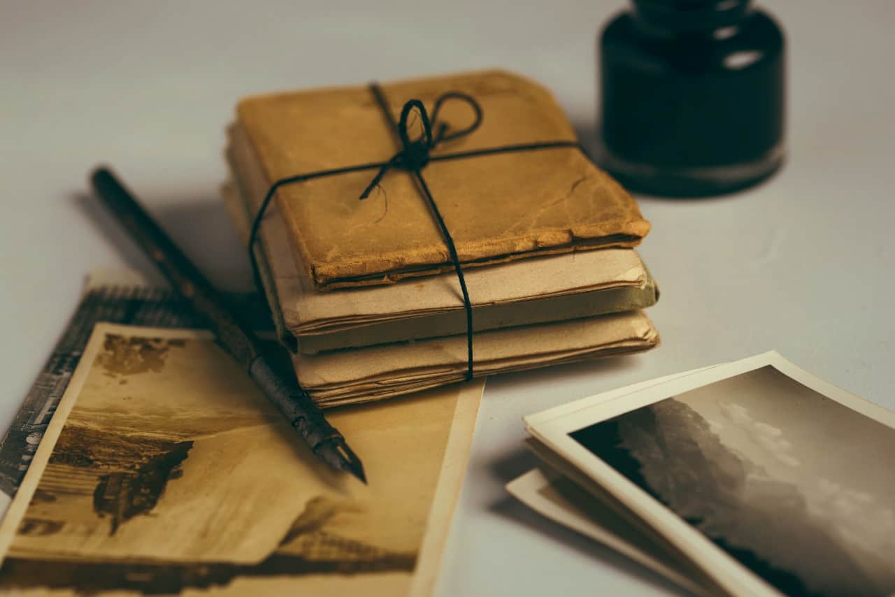 A stack of letters, a fountain pin, a jar of ink, and old photos.