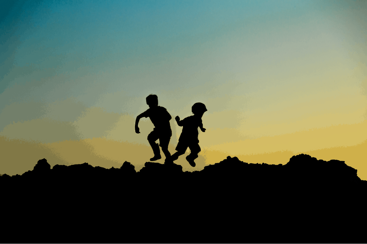 2 silhouettes of boys playing on rocks at sunset.