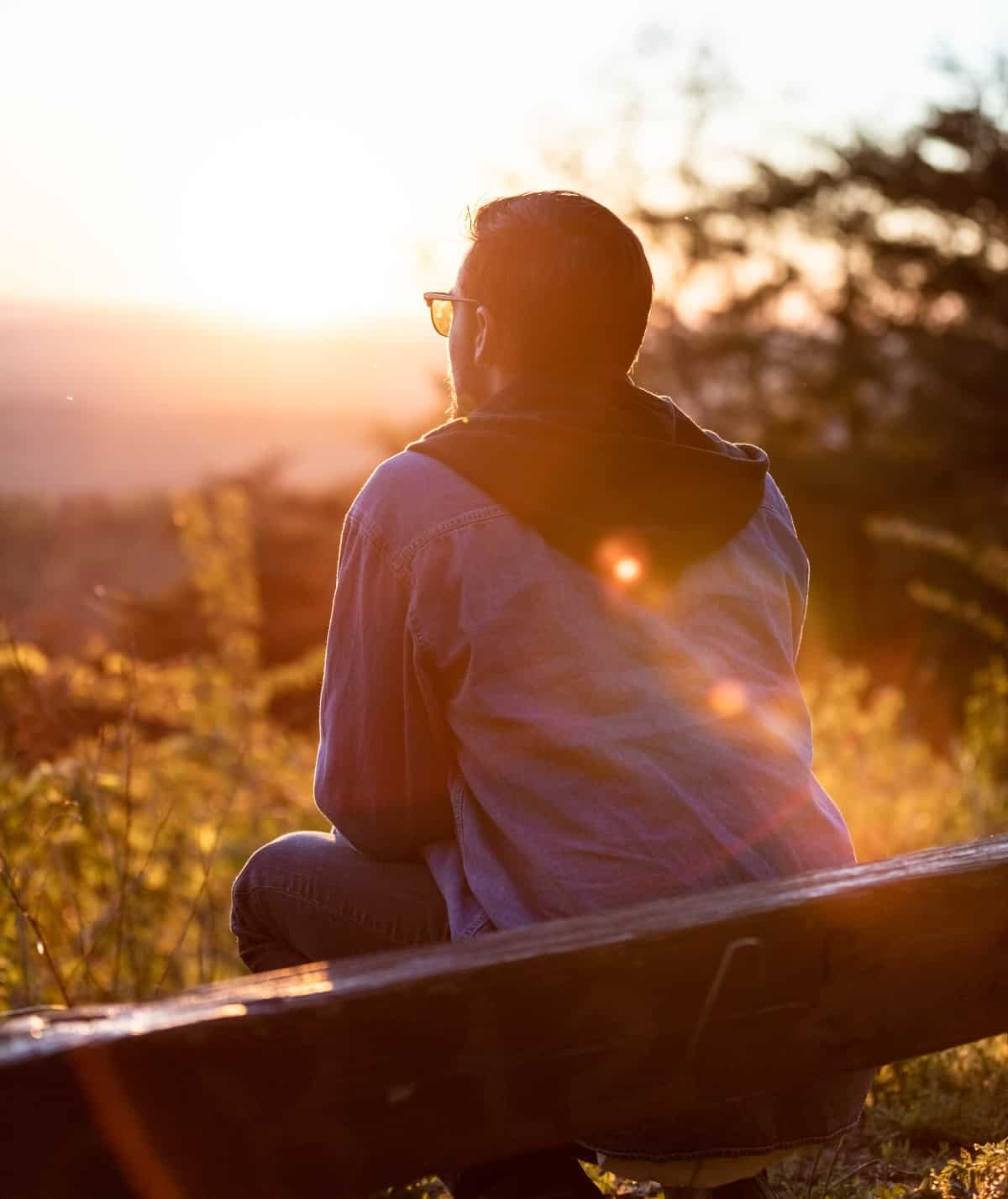 A man sitting on a bench at sunset.