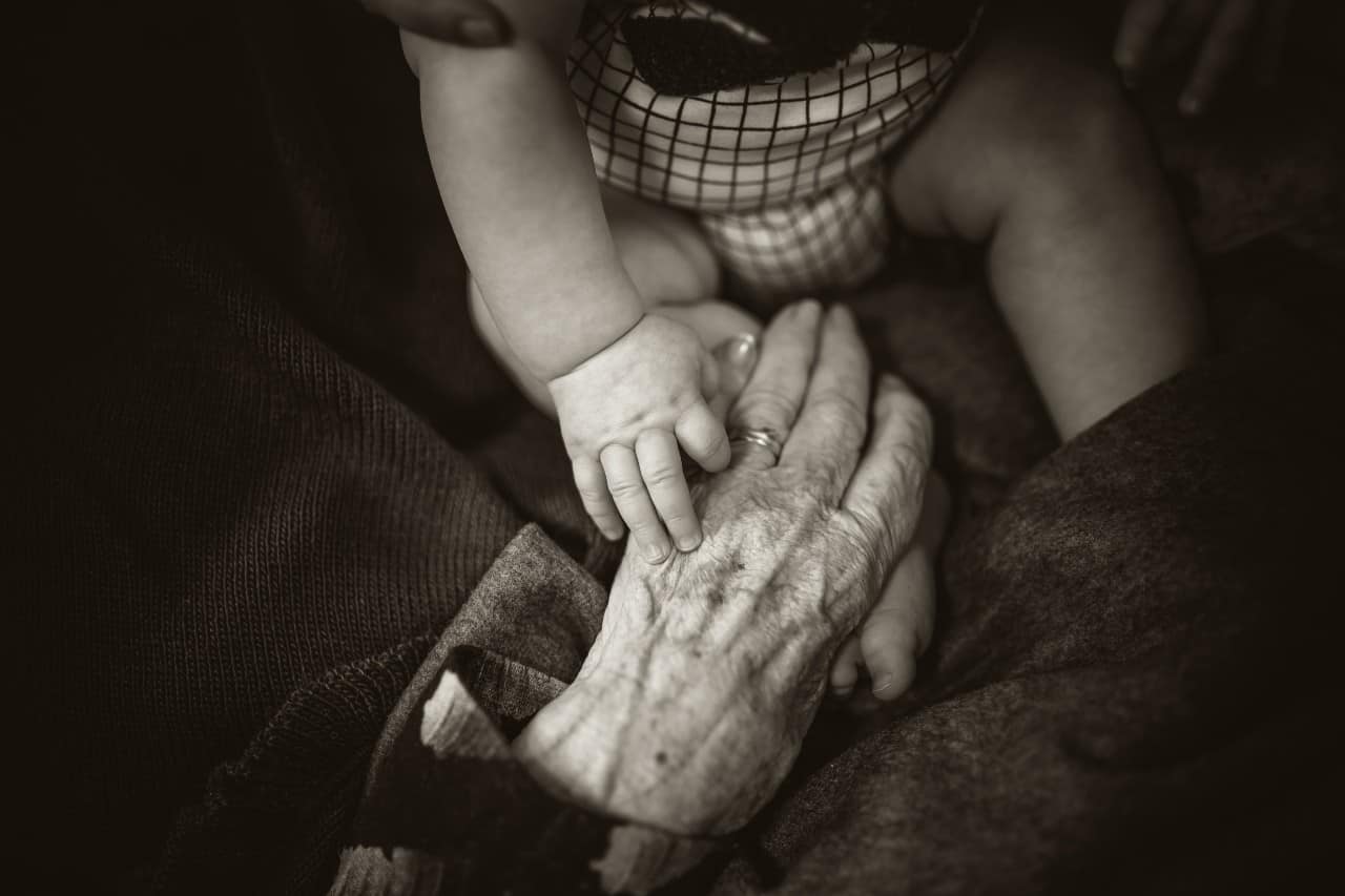 A baby holding the hand of a grandparent.