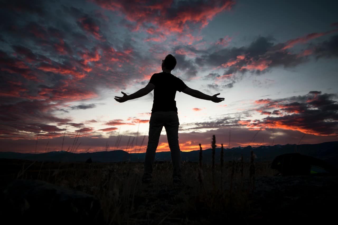 Silhouette of a man at sunset with his arms wide open.
