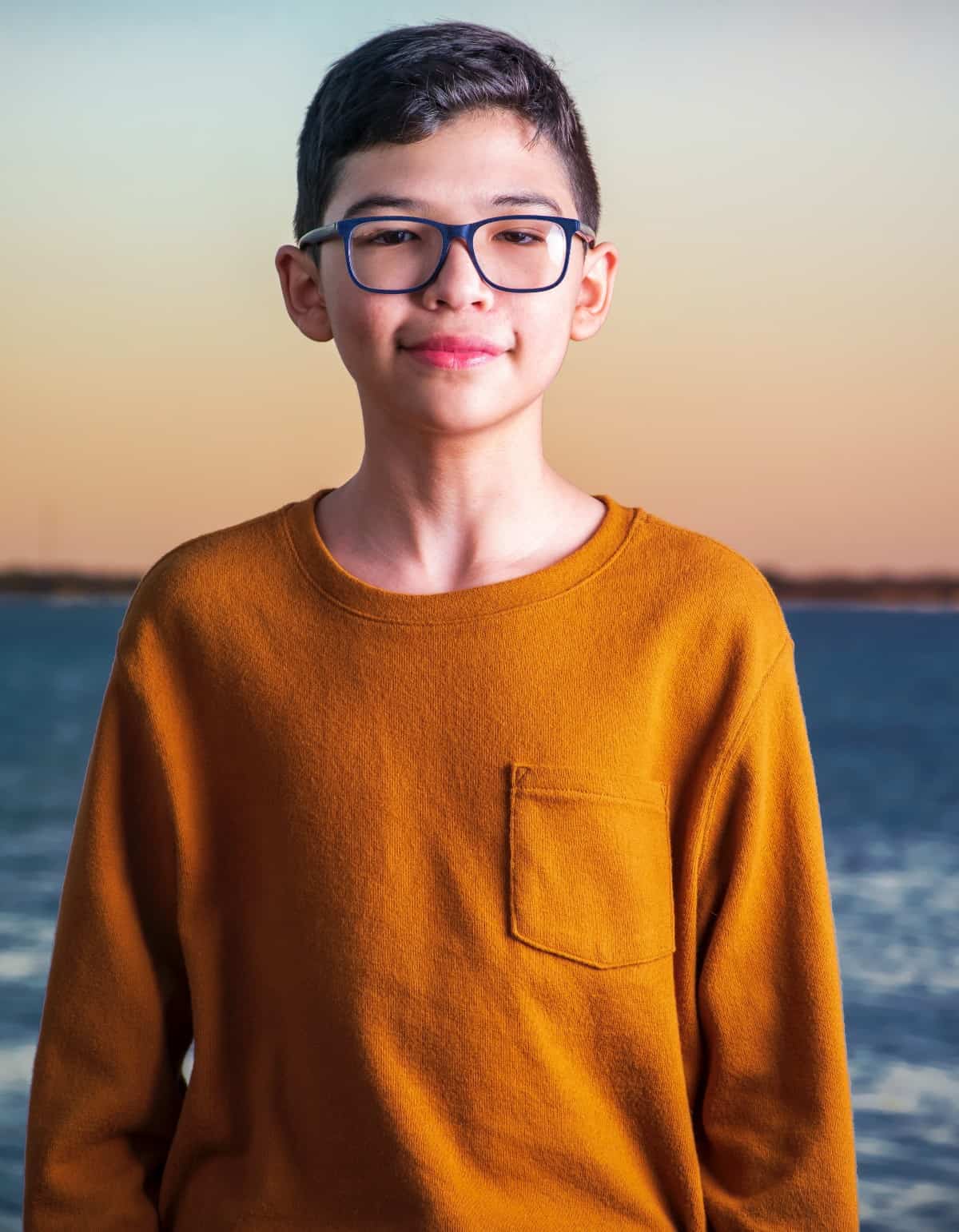 A young boy wearing glasses and smiling at the camera.