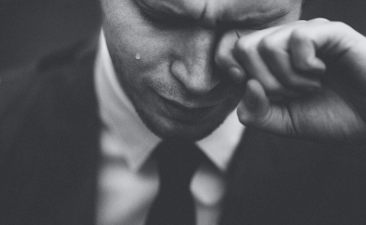 A man in a suit wiping a tear from his eye.