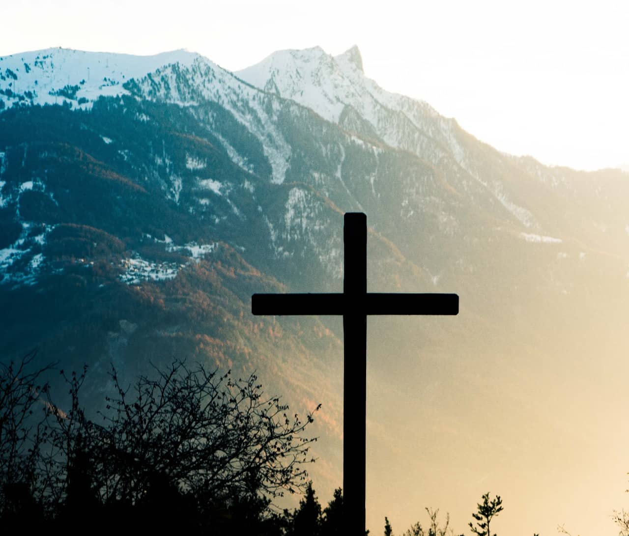 A photo of a wooden cross in front of a mountain.