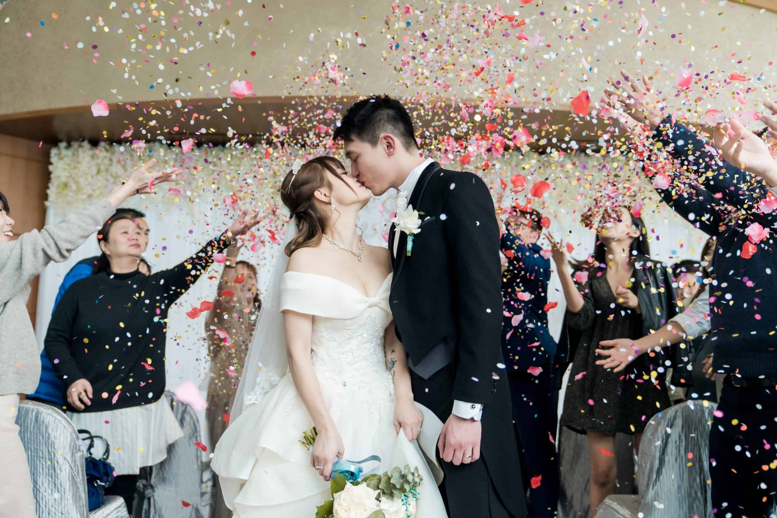 bride and groom kissing with confetti thrown by wedding guests