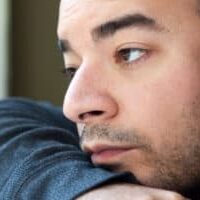 Close up of an unshaven depressed young man gazing off into the distance. Shallow depth of field.