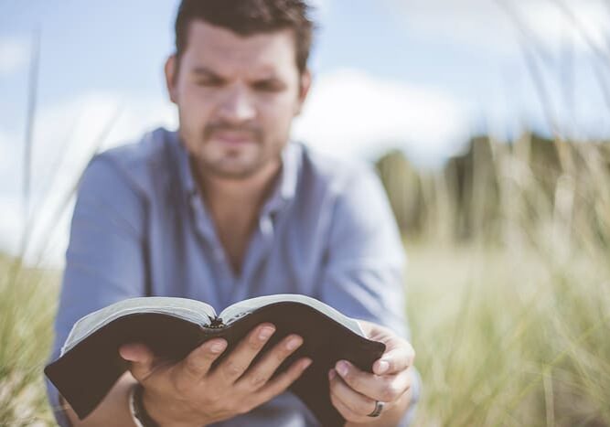 Man outside reading Bible.