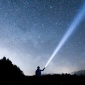 Man with flashlight into the night sky