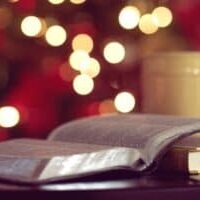An open Bible with a cup of coffee and a lit Christmas tree in the background.