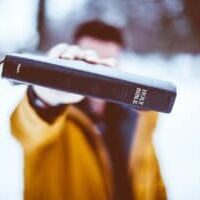 A man Holding a Bible up to the camera in front of his face.