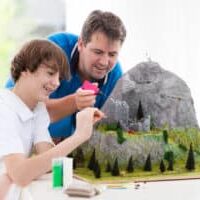 Father and son work on model building school project. Kids and parent build miniature scale model mountain for geography class. Extracurricular activities and family hobby. Art and crafts for child.