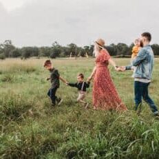 A family of five walking through a field holding hands.