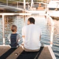 Father and son sitting on a dock looking out at the water.