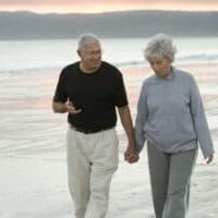 older-man-and-wife-holding-hands-on-beach