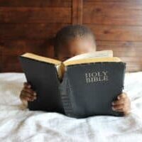 A little boy laying in bed and reading the Bible.