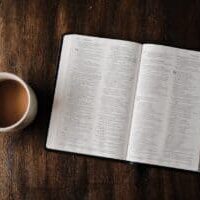 A cup of coffee next to an open Bible.