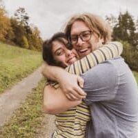 A man and woman hugging next to a road near a wooded area.